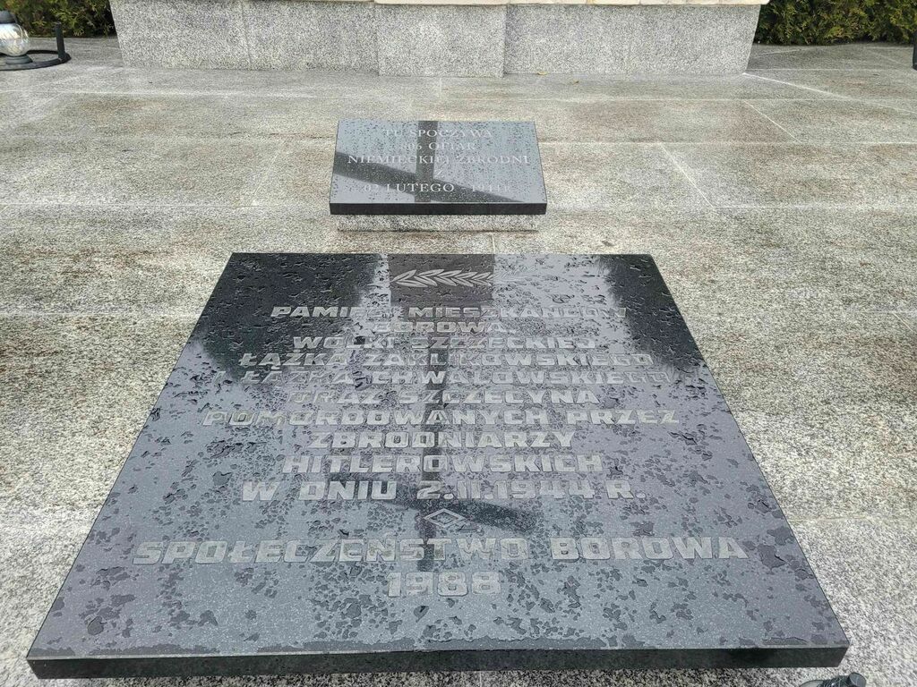 
                                                    Płyta nagrobna na mogile z inskrypcją upamiętniającą ofiary pacyfikacji z 1944 r., umieszczona na kamiennym fundamencie.
                                                
