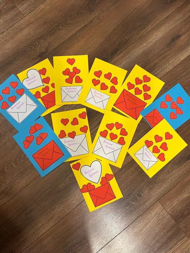 
                                                    Kolorowe kartki papieru z kopertami i serduszkami na drewnianej podłodze. Każda kartka ma napis związany z wyzwaniem „Szanuję innych – to moja supermoc”, w tym „Tworzymy przyjaźń” i „Jesteś wyjątkowy”.
                                                