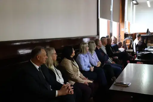 Szkolenie w sali konferencyjnej wyłożonej ciemnym drewnem: mężczyźni z mikrofonem przemawiają przy stole prezydialnym na tle godła Polski, herbu i mapy Powiatu Lubelskiego oraz flag, uczestnicy siedzą na krzesłach i słuchają, na ekranie widać slajd z napisem Zagrożenie z powietrza, szkolenie, Starostwo Powiatowe Lublin, 7 października 2026 rok, a kilkanaście osób pozuje do wspólnej fotografii na schodach podestu.