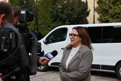 Przekazanie białego busa Renault Trafic z czerwoną kokardą przed budynkiem Starostwa Powiatowego w Lublinie: winda w tylnych drzwiach, wywiady dla telewizji, wspólne zdjęcia z podopiecznymi i spotkanie przy stole w sali.