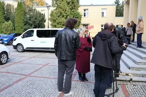 Przekazanie białego busa Renault Trafic z czerwoną kokardą przed budynkiem Starostwa Powiatowego w Lublinie: winda w tylnych drzwiach, wywiady dla telewizji, wspólne zdjęcia z podopiecznymi i spotkanie przy stole w sali.