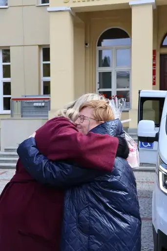 Przekazanie białego busa Renault Trafic z czerwoną kokardą przed budynkiem Starostwa Powiatowego w Lublinie: winda w tylnych drzwiach, wywiady dla telewizji, wspólne zdjęcia z podopiecznymi i spotkanie przy stole w sali.