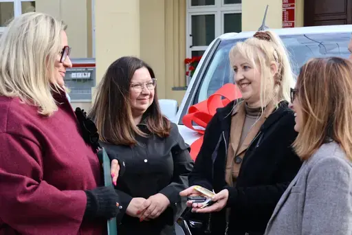 Przekazanie białego busa Renault Trafic z czerwoną kokardą przed budynkiem Starostwa Powiatowego w Lublinie: winda w tylnych drzwiach, wywiady dla telewizji, wspólne zdjęcia z podopiecznymi i spotkanie przy stole w sali.
