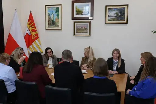 Przekazanie białego busa Renault Trafic z czerwoną kokardą przed budynkiem Starostwa Powiatowego w Lublinie: winda w tylnych drzwiach, wywiady dla telewizji, wspólne zdjęcia z podopiecznymi i spotkanie przy stole w sali.