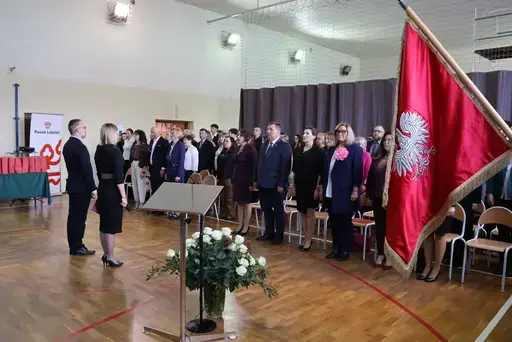 Obchody Powiatowego Dnia Edukacji Narodowej w sali gimnastycznej szkoły w Bełżycach: wystąpienia przy mównicy, wręczanie dyplomów i upominków nauczycielom oraz uczniom, goście na widowni, poczet sztandarowy i występ muzyczny uczniów.