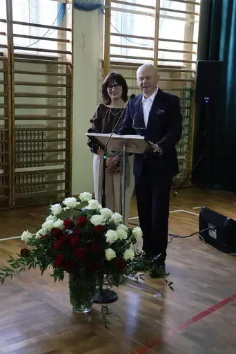 Obchody Powiatowego Dnia Edukacji Narodowej w sali gimnastycznej szkoły w Bełżycach: wystąpienia przy mównicy, wręczanie dyplomów i upominków nauczycielom oraz uczniom, goście na widowni, poczet sztandarowy i występ muzyczny uczniów.