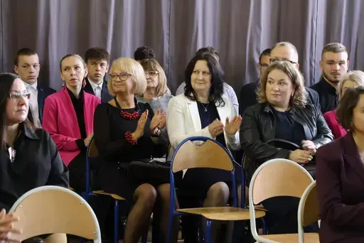 Obchody Powiatowego Dnia Edukacji Narodowej w sali gimnastycznej szkoły w Bełżycach: wystąpienia przy mównicy, wręczanie dyplomów i upominków nauczycielom oraz uczniom, goście na widowni, poczet sztandarowy i występ muzyczny uczniów.