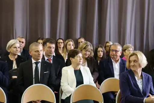 Obchody Powiatowego Dnia Edukacji Narodowej w sali gimnastycznej szkoły w Bełżycach: wystąpienia przy mównicy, wręczanie dyplomów i upominków nauczycielom oraz uczniom, goście na widowni, poczet sztandarowy i występ muzyczny uczniów.