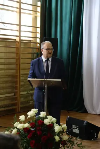 Obchody Powiatowego Dnia Edukacji Narodowej w sali gimnastycznej szkoły w Bełżycach: wystąpienia przy mównicy, wręczanie dyplomów i upominków nauczycielom oraz uczniom, goście na widowni, poczet sztandarowy i występ muzyczny uczniów.