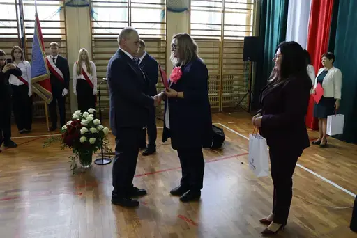 Obchody Powiatowego Dnia Edukacji Narodowej w sali gimnastycznej szkoły w Bełżycach: wystąpienia przy mównicy, wręczanie dyplomów i upominków nauczycielom oraz uczniom, goście na widowni, poczet sztandarowy i występ muzyczny uczniów.