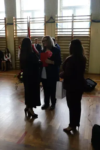 Obchody Powiatowego Dnia Edukacji Narodowej w sali gimnastycznej szkoły w Bełżycach: wystąpienia przy mównicy, wręczanie dyplomów i upominków nauczycielom oraz uczniom, goście na widowni, poczet sztandarowy i występ muzyczny uczniów.