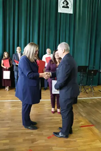 Obchody Powiatowego Dnia Edukacji Narodowej w sali gimnastycznej szkoły w Bełżycach: wystąpienia przy mównicy, wręczanie dyplomów i upominków nauczycielom oraz uczniom, goście na widowni, poczet sztandarowy i występ muzyczny uczniów.