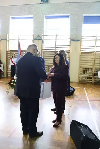 Obchody Powiatowego Dnia Edukacji Narodowej w sali gimnastycznej szkoły w Bełżycach: wystąpienia przy mównicy, wręczanie dyplomów i upominków nauczycielom oraz uczniom, goście na widowni, poczet sztandarowy i występ muzyczny uczniów.