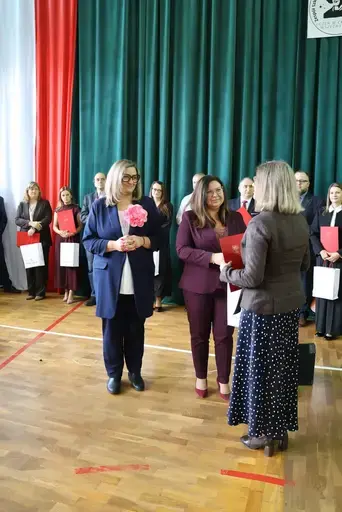 Obchody Powiatowego Dnia Edukacji Narodowej w sali gimnastycznej szkoły w Bełżycach: wystąpienia przy mównicy, wręczanie dyplomów i upominków nauczycielom oraz uczniom, goście na widowni, poczet sztandarowy i występ muzyczny uczniów.