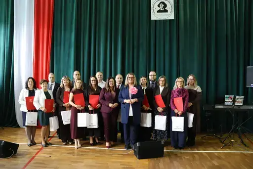 Obchody Powiatowego Dnia Edukacji Narodowej w sali gimnastycznej szkoły w Bełżycach: wystąpienia przy mównicy, wręczanie dyplomów i upominków nauczycielom oraz uczniom, goście na widowni, poczet sztandarowy i występ muzyczny uczniów.