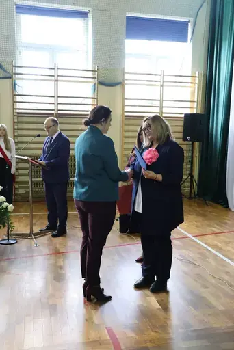 Obchody Powiatowego Dnia Edukacji Narodowej w sali gimnastycznej szkoły w Bełżycach: wystąpienia przy mównicy, wręczanie dyplomów i upominków nauczycielom oraz uczniom, goście na widowni, poczet sztandarowy i występ muzyczny uczniów.