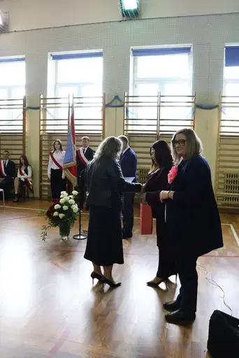 Obchody Powiatowego Dnia Edukacji Narodowej w sali gimnastycznej szkoły w Bełżycach: wystąpienia przy mównicy, wręczanie dyplomów i upominków nauczycielom oraz uczniom, goście na widowni, poczet sztandarowy i występ muzyczny uczniów.