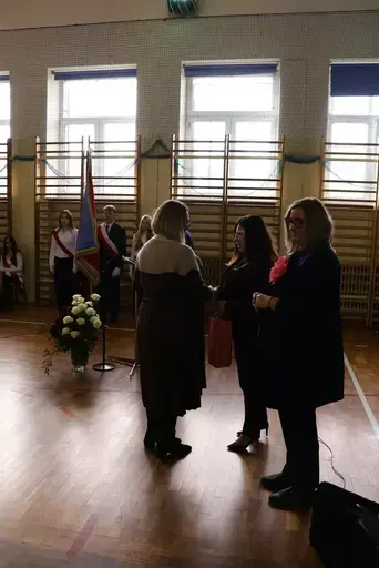 Obchody Powiatowego Dnia Edukacji Narodowej w sali gimnastycznej szkoły w Bełżycach: wystąpienia przy mównicy, wręczanie dyplomów i upominków nauczycielom oraz uczniom, goście na widowni, poczet sztandarowy i występ muzyczny uczniów.