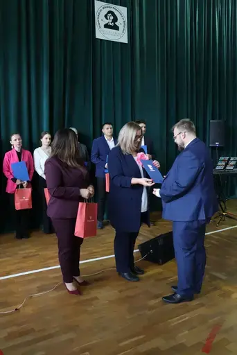 Obchody Powiatowego Dnia Edukacji Narodowej w sali gimnastycznej szkoły w Bełżycach: wystąpienia przy mównicy, wręczanie dyplomów i upominków nauczycielom oraz uczniom, goście na widowni, poczet sztandarowy i występ muzyczny uczniów.