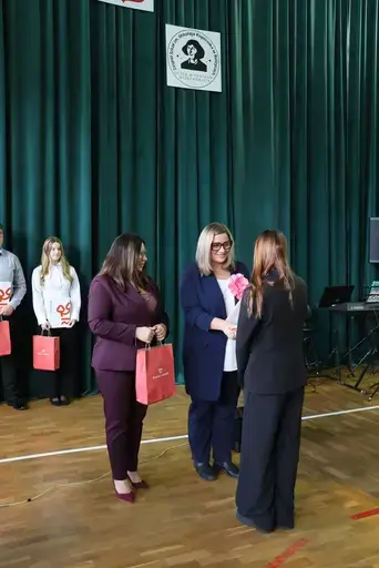 Obchody Powiatowego Dnia Edukacji Narodowej w sali gimnastycznej szkoły w Bełżycach: wystąpienia przy mównicy, wręczanie dyplomów i upominków nauczycielom oraz uczniom, goście na widowni, poczet sztandarowy i występ muzyczny uczniów.