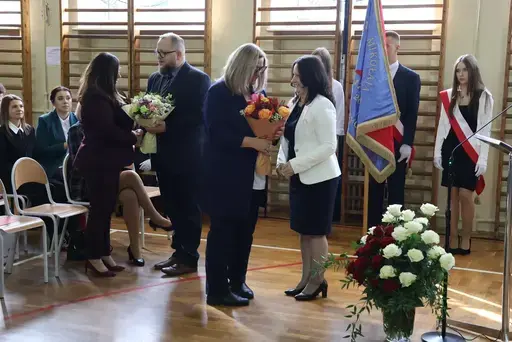 Obchody Powiatowego Dnia Edukacji Narodowej w sali gimnastycznej szkoły w Bełżycach: wystąpienia przy mównicy, wręczanie dyplomów i upominków nauczycielom oraz uczniom, goście na widowni, poczet sztandarowy i występ muzyczny uczniów.
