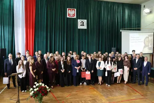 Obchody Powiatowego Dnia Edukacji Narodowej w sali gimnastycznej szkoły w Bełżycach: wystąpienia przy mównicy, wręczanie dyplomów i upominków nauczycielom oraz uczniom, goście na widowni, poczet sztandarowy i występ muzyczny uczniów.