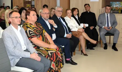 
                                                    Uczestnicy powiatowych obchodów Światowego Dnia Zdrowia Psychicznego w sali Ośrodka Wsparcia w Leopoldowie: goście i publiczność na krzesłach, prelegenci z mikrofonem przy ekranie projekcyjnym oraz występujący na tle granatowego banera z nazwą wydarzenia, ozdobionego kolorowymi jesiennymi liśćmi.
                                                