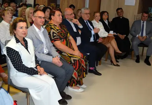 
                                                    Uczestnicy powiatowych obchodów Światowego Dnia Zdrowia Psychicznego w sali Ośrodka Wsparcia w Leopoldowie: goście i publiczność na krzesłach, prelegenci z mikrofonem przy ekranie projekcyjnym oraz występujący na tle granatowego banera z nazwą wydarzenia, ozdobionego kolorowymi jesiennymi liśćmi.
                                                