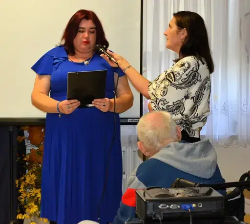 
                                                    Uczestnicy powiatowych obchodów Światowego Dnia Zdrowia Psychicznego w sali Ośrodka Wsparcia w Leopoldowie: goście i publiczność na krzesłach, prelegenci z mikrofonem przy ekranie projekcyjnym oraz występujący na tle granatowego banera z nazwą wydarzenia, ozdobionego kolorowymi jesiennymi liśćmi.
                                                