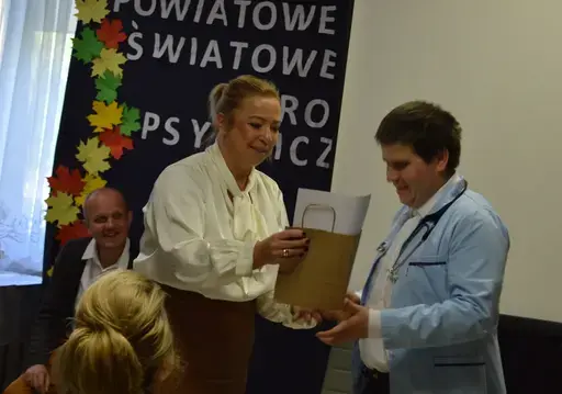 
                                                    Uczestnicy powiatowych obchodów Światowego Dnia Zdrowia Psychicznego w sali Ośrodka Wsparcia w Leopoldowie: goście i publiczność na krzesłach, prelegenci z mikrofonem przy ekranie projekcyjnym oraz występujący na tle granatowego banera z nazwą wydarzenia, ozdobionego kolorowymi jesiennymi liśćmi.
                                                