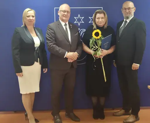 
                                                    Uroczystość w Starostwie Powiatowym w Rykach. Nagrodzeni nauczyciele i pracownicy oświaty z kwiatami i dyplomami pozują z władzami powiatu na tle granatowej ścianki z napisem Powiat Rycki.
                                                
