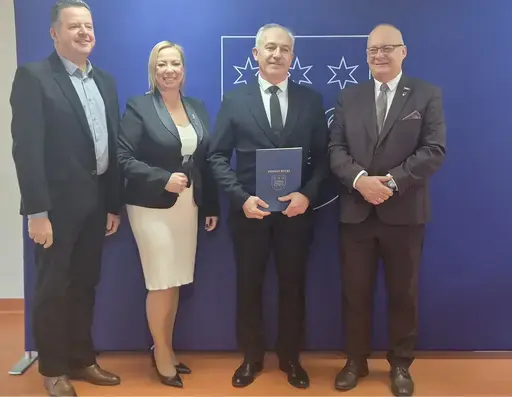 
                                                    Uroczystość w Starostwie Powiatowym w Rykach. Nagrodzeni nauczyciele i pracownicy oświaty z kwiatami i dyplomami pozują z władzami powiatu na tle granatowej ścianki z napisem Powiat Rycki.
                                                
