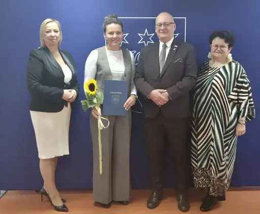 
                                                    Uroczystość w Starostwie Powiatowym w Rykach. Nagrodzeni nauczyciele i pracownicy oświaty z kwiatami i dyplomami pozują z władzami powiatu na tle granatowej ścianki z napisem Powiat Rycki.
                                                