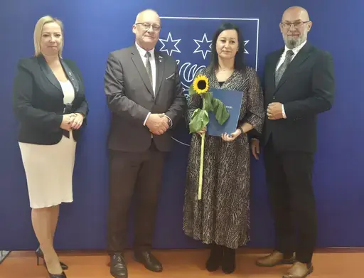 
                                                    Uroczystość w Starostwie Powiatowym w Rykach. Nagrodzeni nauczyciele i pracownicy oświaty z kwiatami i dyplomami pozują z władzami powiatu na tle granatowej ścianki z napisem Powiat Rycki.
                                                