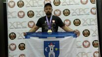 Bartłomiej Rogoziński Mistrz Europy i Świata w wyciskaniu sztangi leżąc prezentuje flagę Świebodzic