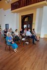 Zdjęcie przedstawia publicznośc zgromadzoną na spotkaniu autorskim, słuchającą prelakcji. Na pierwsz