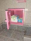 Zdjęcie przedstawia niedużą, różową, metalową szafkę z otwartym drzwiami.
