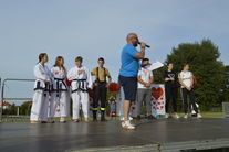 Mężczyzna na scenie, za nim grupa uczestników pokazów karate