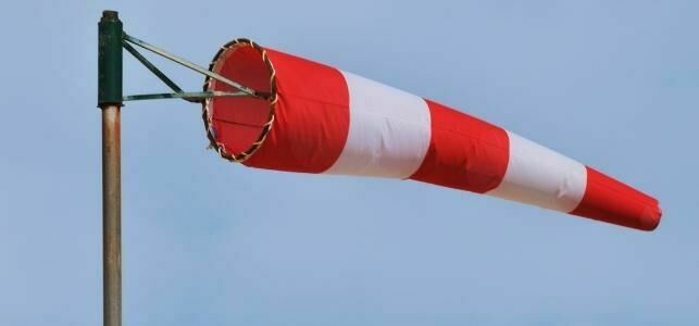 Czerwono-biały rękaw wiatrowy napompowany wiatrem na tle niebieskiego nieba, zamocowany na metalowym uchwycie.