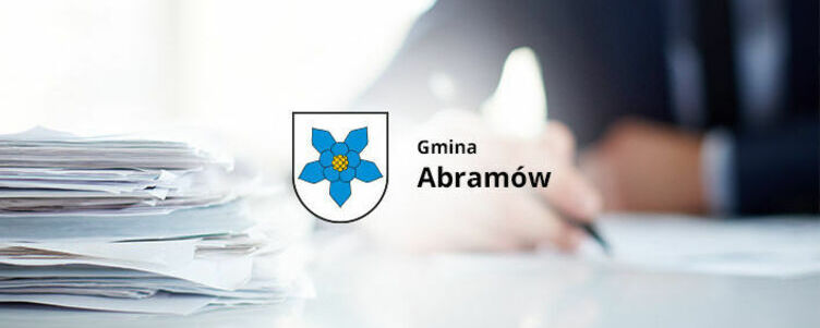 Osoba w biurze pracuje przy dokumentach z logo "Gmina Abramów" na przedzie, w tle rozmyte.