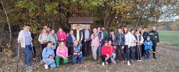 Grupa ludzi gromadzi się na zewnątrz wśród drzew, niektórzy z kijkami do nordic walking, uśmiechnięci, w dziennym świetle.