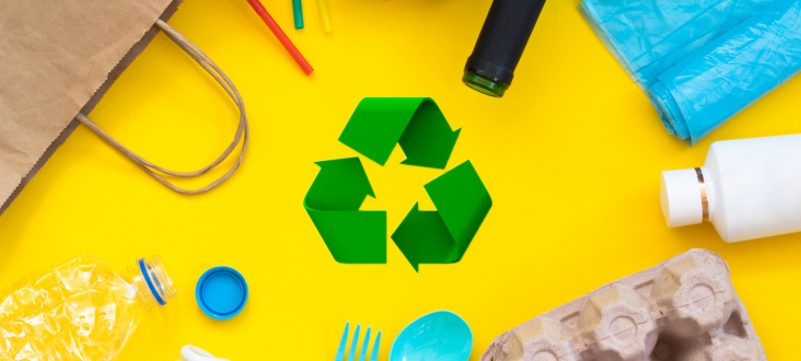 Na żółtym tle symbol recyklingu otoczony przedmiotami do recyklingu: butelkami, kartonem, widelcem plastikowym.