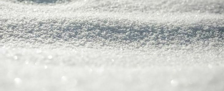 Zdjęcie zbliżenia błyszczącej, skrystalizowanej powierzchni śniegu z widocznymi śnieżnymi ziarnami i delikatnymi odblaskami światła.