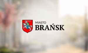 Logo miasta Brańsk z herbem przedstawiającym postać trzymającą tarczę, na tle rozmytego zdjęcia ulicy.