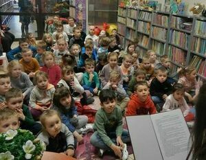 Na zdjęciu dzieci, które siedzą na dywanie i słuchają pani.