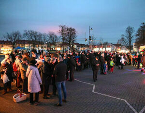 Zdjęcie przedstawia tłum ludzi zgromadzonych wieczorem na miejskim placu, z elementami oświetlonymi, co wskazuje na specjalne wydarzenie lub zgromadzenie.