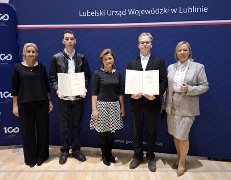 Grupa czterech osób stoi przed ścianą z logo i napisem "Lubelski Urząd Wojewódzki w Lublinie", trzymają dokumenty.