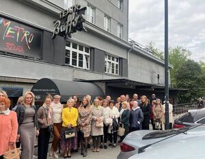 Grupa osób stoi przed budynkiem teatru. Nad wejściem widoczny jest napis "Teatr Buffo" oraz transparent "Metro 32 lata". Ludzie pozują do zdjęcia w pogodny dzień.