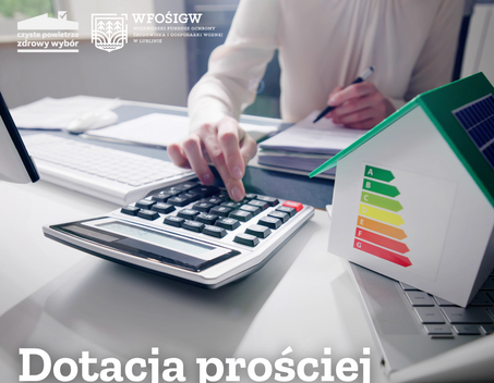 Ręka naciska przycisk kalkulatora na biurku. Obok znajduje się model domu z kolorową etykietą energetyczną. W lewym górnym rogu logo WFOŚiGW. Na dole napis: "Dotacja prościej niż myślisz".