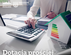 Ręka naciska przycisk kalkulatora na biurku. Obok znajduje się model domu z kolorową etykietą energetyczną. W lewym górnym rogu logo WFOŚiGW. Na dole napis: "Dotacja prościej niż myślisz".